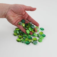 Video of green mix glass nuggets in lime, grass and emerald green shades with an iridescent sheen, 16–20 mm, picked up from a pile by hand and dropped back to show their size, round shape and shine